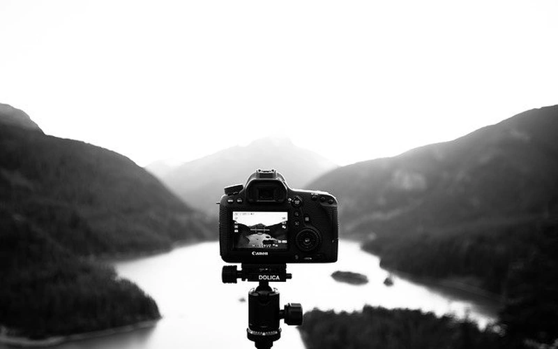Professional camera mounted on a tripod overlooking a scenic mountain lake landscape