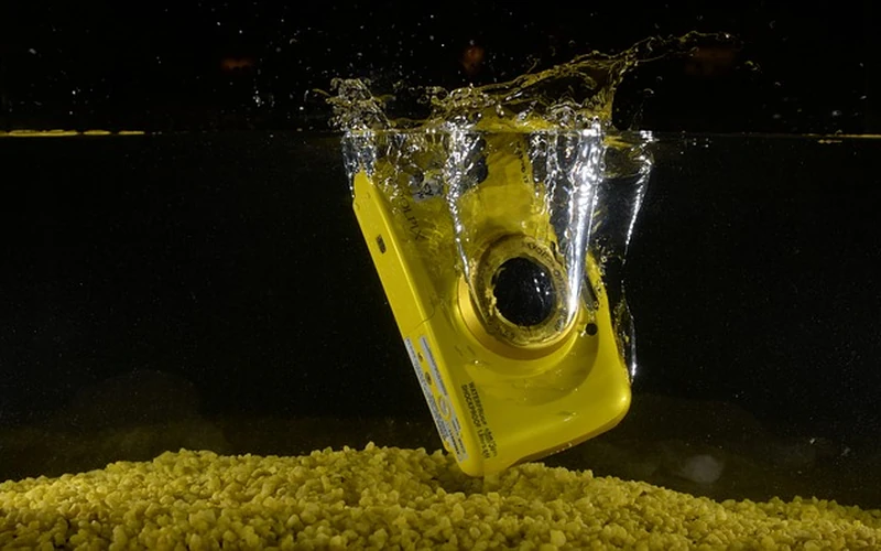 Rugged waterproof underwater camera splashing into clear water above a pebble seabed
